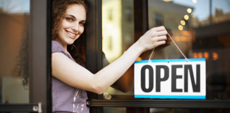 Giovane imprenditrice appende il cartello Open alla porta del suo esercizio commerciale