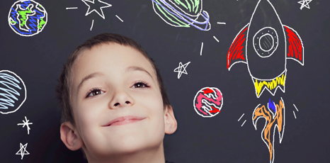 Un bambino sorride davanti a una lavagna con disegni di navette spaziali e pianeti