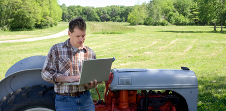 Agricoltore poggiato a un trattore scrive su un computer