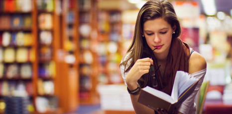 Una ragazza legge un libro dentro una biblioteca