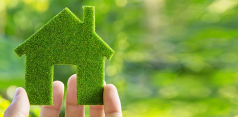 Immagine di una piccola casa stilizzata in tessuto sintetico verde tenuta da una mano, sfondo con sfumature di verde