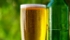 Bicchiere di birra pieno accanto a bottiglia di vetro verde