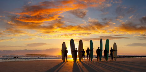 Persone con tavole da surf su una spiaggia al tramonto